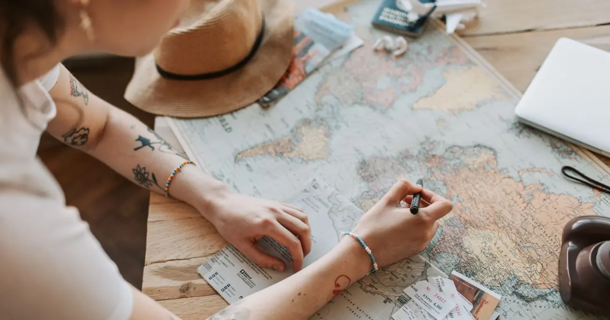 Persona planificando un viaje con un mapa, un pasaporte y objetos de viaje sobre una mesa de madera
