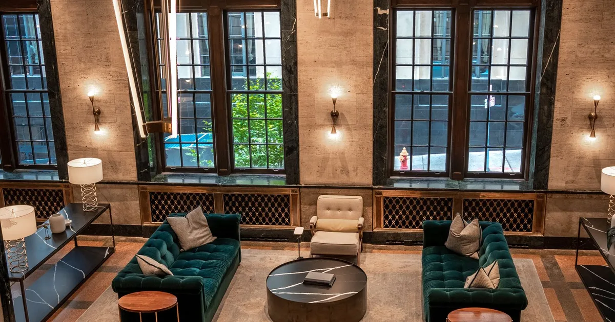 Vestíbulo elegante de un hotel con sofás verdes, lámparas y grandes ventanales